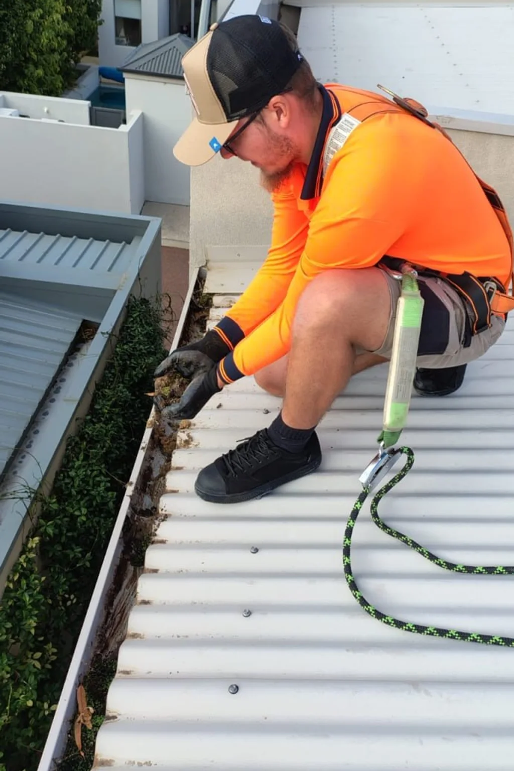 Gutter cleaner clearing leaves from a flat carport gutter at a Perth home