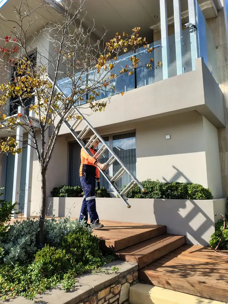 Gutter cleaning technician carrying a ladder to access a double-storey Perth home