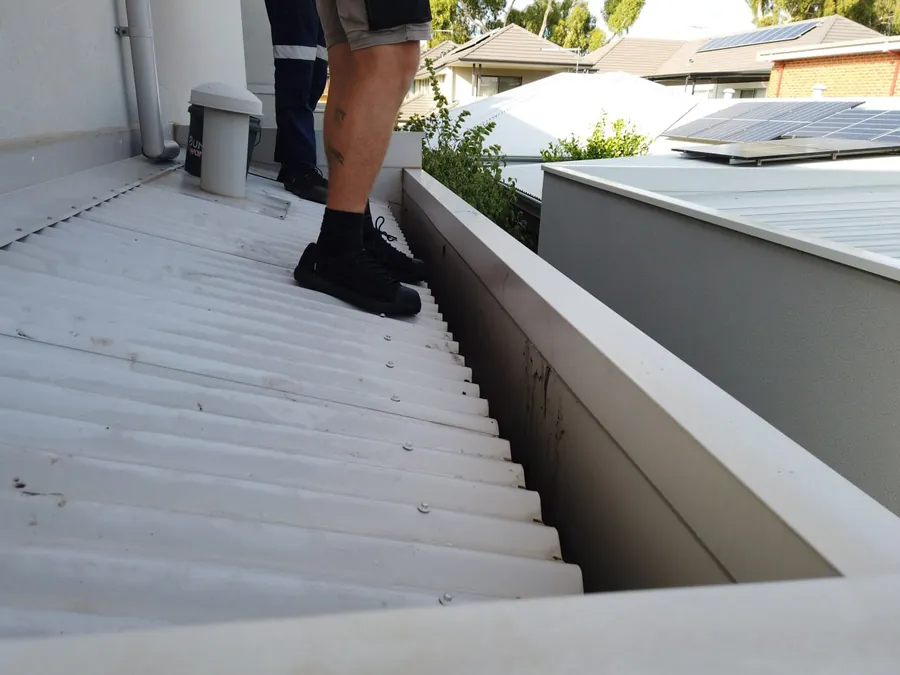 Gutter cleaning technician working safely at height with a harness on a Perth roof